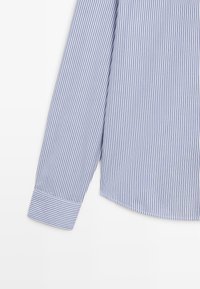 Lichtblauwe shirt met verticale navy strepen, lange mouwen, knoopmanchetten en een afgeronde zoom; gemaakt van een gladde stof.