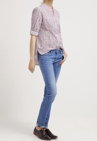 Chemise à manches longues à motifs rouges et blancs avec un col, associée à un jean skinny bleu clair et des chaussures à lacets marron foncé.