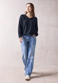 Zwarte hoodie met textuur en trekkoorden, gecombineerd met lichtblauwe rechtpattern jeans. Witte sneakers maken de casual outfit compleet.