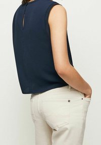 Canotta blu navy senza maniche con una finitura testurizzata e dettaglio a chiave sul retro, abbinata a jeans fitted di colore chiaro.
