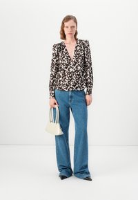 Donna che indossa una blusa a righe bianco e nero, jeans larghi blu, scarpe nere a punta, mentre tiene in mano una piccola borsa bianca.