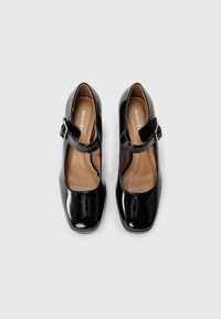 Black patent leather Mary Jane shoes with a square toe, single strap, and adjustable buckle. Interior features a tan lining.