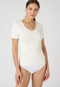 Camiseta de manga corta en crema con escote en V, confeccionada en una tela suave y lisa, que presenta una forma ajustada y costuras sutiles alrededor del escote.