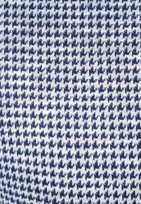 Granatowa i biała dzianina z małym wzorem w zębatkę, charakteryzująca się teksturowanym wyglądem i gęstym, równomiernym splotem.