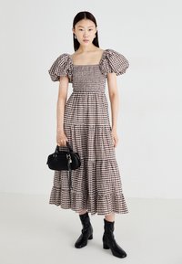Bruin en wit geruite jurk met korte pofmouwen, meerlagige rok, getailleerde taille, gecombineerd met een zwarte handtas en zwarte laarzen met hak.