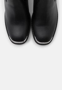 Stivaletti neri in pelle con punta arrotondata, caratterizzati da una texture liscia e un accento argentato lucido sulla punta.