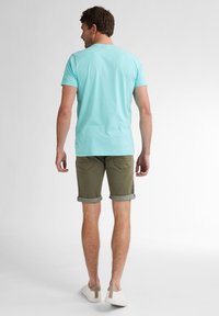T-shirt en coton bleu clair à manches courtes, associé à un short vert olive avec des ourlets roulés. Le modèle porte des chaussures blanches avec des accents beiges.