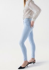 Jeans ajustados de color azul claro con una cintura alta, combinados con una camisa blanca con lunares negros y tacones tipo slingback negros.
