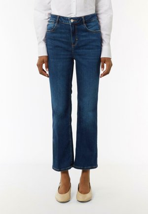 Donkerblauwe denim jeans met een rechte pijp, vijf zakken en contrasterende oranje steken. Draag ze met lichtgekleurde flats.