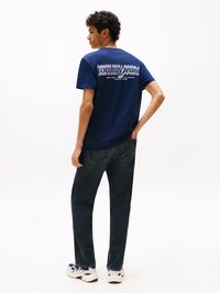 Tumši zila kokvilnas T-krekls ar krāsainu "tommy jeans" grafiku uz aizmugures. Apvienots ar tumšiem džinsu biksēm un baltām kedām.