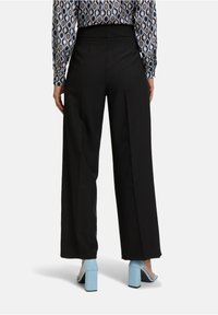 Czarne spodnie z szerokimi nogawkami i wysokim stanem, z dopasowanymi plisaami i gładką teksturą; zestawione z jasnoniebieskimi butami na blokowym obcasie.