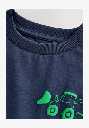 Granatowa bluza z dekoltem ściąganym; z przodu znajduje się jasna zielona grafika traktora; materiał bawełniany o gładkiej fakturze.