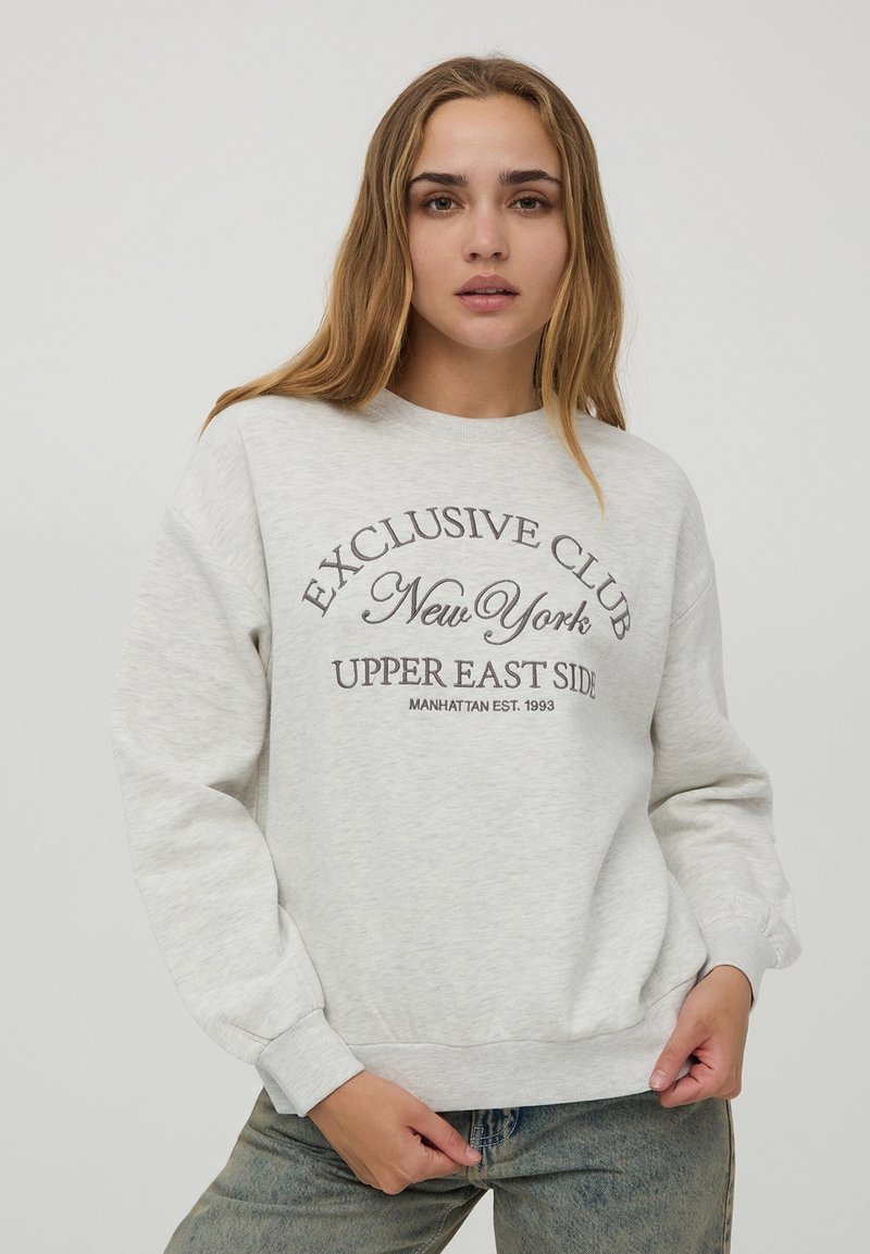 Felpa grigia con scollatura tonda e maniche lunghe. Sul davanti c'è la scritta "Exclusive Club New York Upper East Side". Materiale in misto cotone.