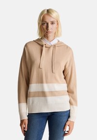 Sweat à capuche beige avec des rayures blanches et marron clair, des poignets et un ourlet côtelés, et un cordon de serrage à la capuche. Tissu tricoté doux et texturé.