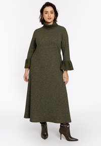 Robe vert olive à manches longues avec un col montant et des poignets évasés, en tissu texturé et pailleté, assortie à des bottines brunes à bout pointu.