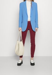 Lichtblauwe blazer, witte top, kastanjebruine skinny broek en zwarte plateau schoenen. Grote crèmekleurige tas. Gladde stof met een geraffineerd ontwerp.