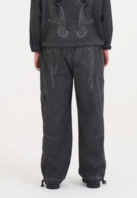 Pantaloni cargo neri con una vestibilità rilassata, caratterizzati da cuciture decorative, tasche laterali e polsini regolabili. Realizzati in un tessuto morbido e testurizzato.