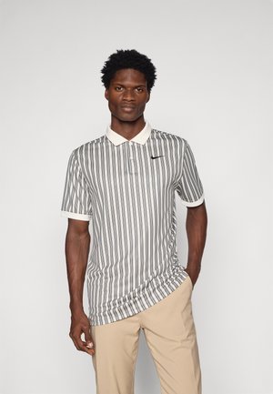 Svītrainā polo krekla baltā, melnā un pelēkā krāsā, ar krēma krāsas apkakli un īsām piedurknēm. Uz krūts ir neliels melns logotips.