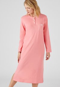 Camicia da notte lunga rosa in morbido tessuto, con collo a bottoni, tasca frontale con pois e spacchi laterali per facilitare i movimenti.