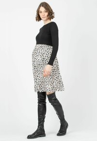 Schwarzes, geripptes Langarmoberteil kombiniert mit einem weißen Rock, der ein schwarz-braunes gepunktetes Muster aufweist. Knielange schwarze Lederstiefel.