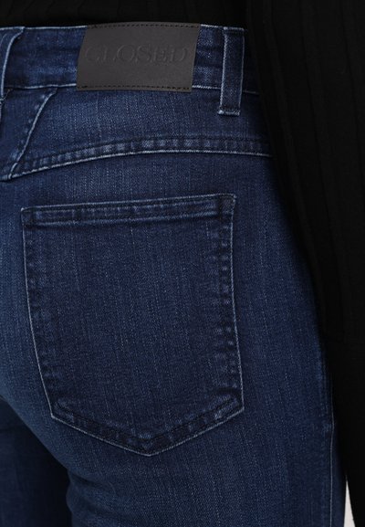 Tmavě modré džíny z denimu s texturovaným povrchem, s obdélníkovou zadní kapsou a černou koženou značkou na pasu.