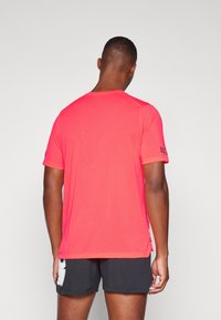 Tricou sportiv roșu din plasă, cu mâneci scurte, având un gât rotund și slituri laterale la tiv pentru o mobilitate crescută.