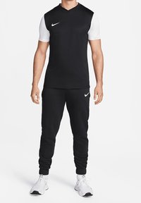 Completo sportivo nero con una maglietta a maniche corte con corpo nero e maniche bianche, abbinato a pantaloni neri e sneakers bianche.