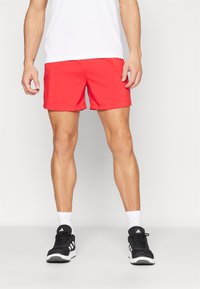 Red athletic shorts with a smooth texture, elastic waistband, and above-knee length, paired with black sports shoes and white socks.