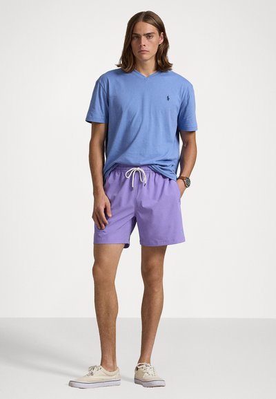 Camiseta azul-claro com decote em V combinada com calções de banho lavanda com cintura elástica e cordão. Ténis bege completam o visual.