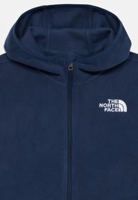 Granatowa polarowa kurtka z kapturem, z przednim zamkiem i białym logo "The North Face" na lewej piersi.