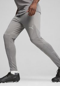 Puma grijze sportleggingen met textuurpanelen en een logo. Gecombineerd met zwarte voetbalschoenen en een grijs shirt, wat een sportieve uitstraling geeft.