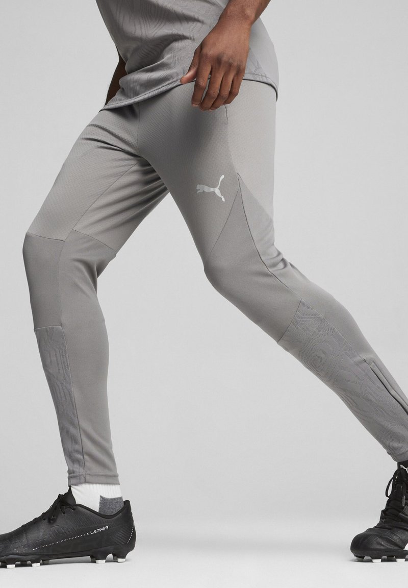 Puma grijze sportleggingen met textuurpanelen en een logo. Gecombineerd met zwarte voetbalschoenen en een grijs shirt, wat een sportieve uitstraling geeft.