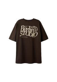 Oversized brun t-shirt lavet af bomuld med en stor grafisk print i cremefarve, der viser tekst og et globusdesign på forsiden.