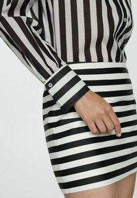 Blusa a rayas en blanco y negro con mangas largas y puños abotonados, combinada con una falda ajustada a rayas en blanco y negro. Textura suave.