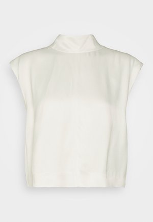 Valkoinen hihaton mock neck -paita, väljelt laskostettu ja suora helma, esillä yksivärisen taustan edessä.