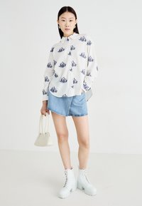 White button-up shirt with blue floral prints, denim skirt, white chunky heeled boots, and a small cream handbag. Smooth fabric and casual design.