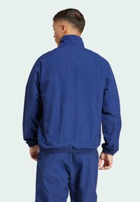 Marinblå vindjacka med elastiska muddar och nederkant, lätt material och hög krage. Inga synliga logotyper eller mönster.