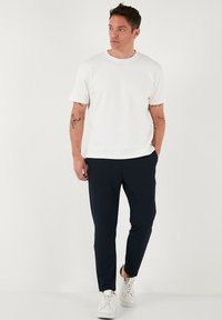 Camiseta blanca de manga corta combinada con pantalones tapered azul marino, con una textura suave. Completado con deportivas blancas.