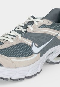 Γκρι και μπεζ αθλητικό παπούτσι Nike με λευκά κορδόνια, πάνελ από δίχτυ και σουέντ, μαλακή σόλα και εμφανές λευκό λογότυπο Swoosh.