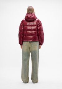 Burgunderfarget, glinsende dunjakke med hette, med horisontale quiltede seksjoner. Kombinert med løse, falmede grønne jeans.