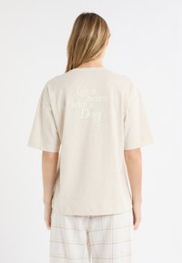 Jasnobeżowa bawełniana koszulka z krótkim rękawem, z centralnie umieszczonym napisem "Życie jest lepsze z psem" w kontrastującym kremowym kolorze.