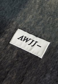 Tissu en feutre gris texturé avec des nuances de noir et de gris clair. Une étiquette rectangulaire blanche avec "AWJJ-" en texte noir en gras est affichée de manière proéminente.