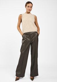 Fuzzy beige mouwloos topje gecombineerd met donkerbruine nep leren wijde broek. De broek heeft een elastische tailleband en een gladde afwerking.