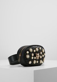 Borse a cintura in pelle nera con zip dorata, decorata con borchie dorate e perle e un'incisione centrale a forma di testa di leopardo dorato.