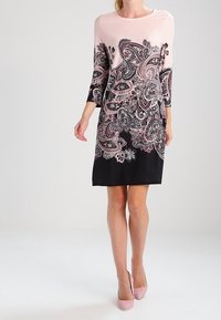 Pencil jurk in roze en zwart met driekwartmouwen, met een paisleypatroon en bloemenaccenten op het lijfje, gladde stof textuur.