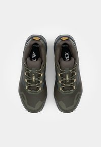 Groene en grijze wandelschoenen hebben een bovenwerk van mesh, een rubberen zool en een versterkte hak, met een camouflagepatroon en contrasterende veters.