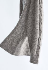 Pull en tricot gris clair avec un motif en grosses mailles texturé sur les manches. Fabriqué en tissu doux et mélangé. Coupe décontractée avec un col rond.