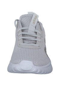 Ljusgrå atletiska sko med nätmaterial, rund tå, snörning framtill och en tjock vit gummisula. Minimalistisk design med logotyp-accent.