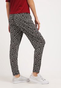 Musta-valkoiset kuviolliset jogginghousut, joissa on kapea malli ja joustava vyötärö, yhdistetty valkoisiin lenkkareihin, jotka esittelevät käsinkirjoitettua tekstiä.