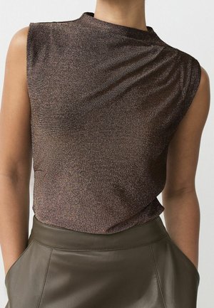 Haut sans manches bronze scintillant associé à un pantalon en cuir vert olive taille haute avec poches latérales, porté par une personne aux bras détendus.
